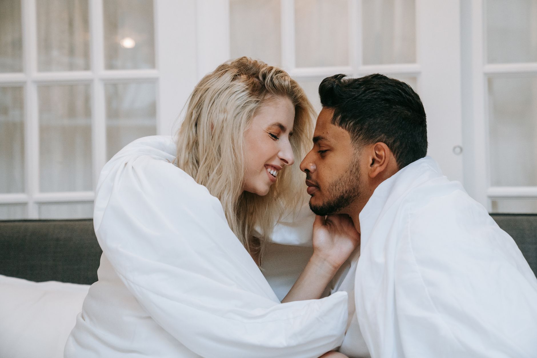 Stel deelt een teder moment onder witte dekens, lichamelijke intimiteit en seks in een liefdevolle relatie